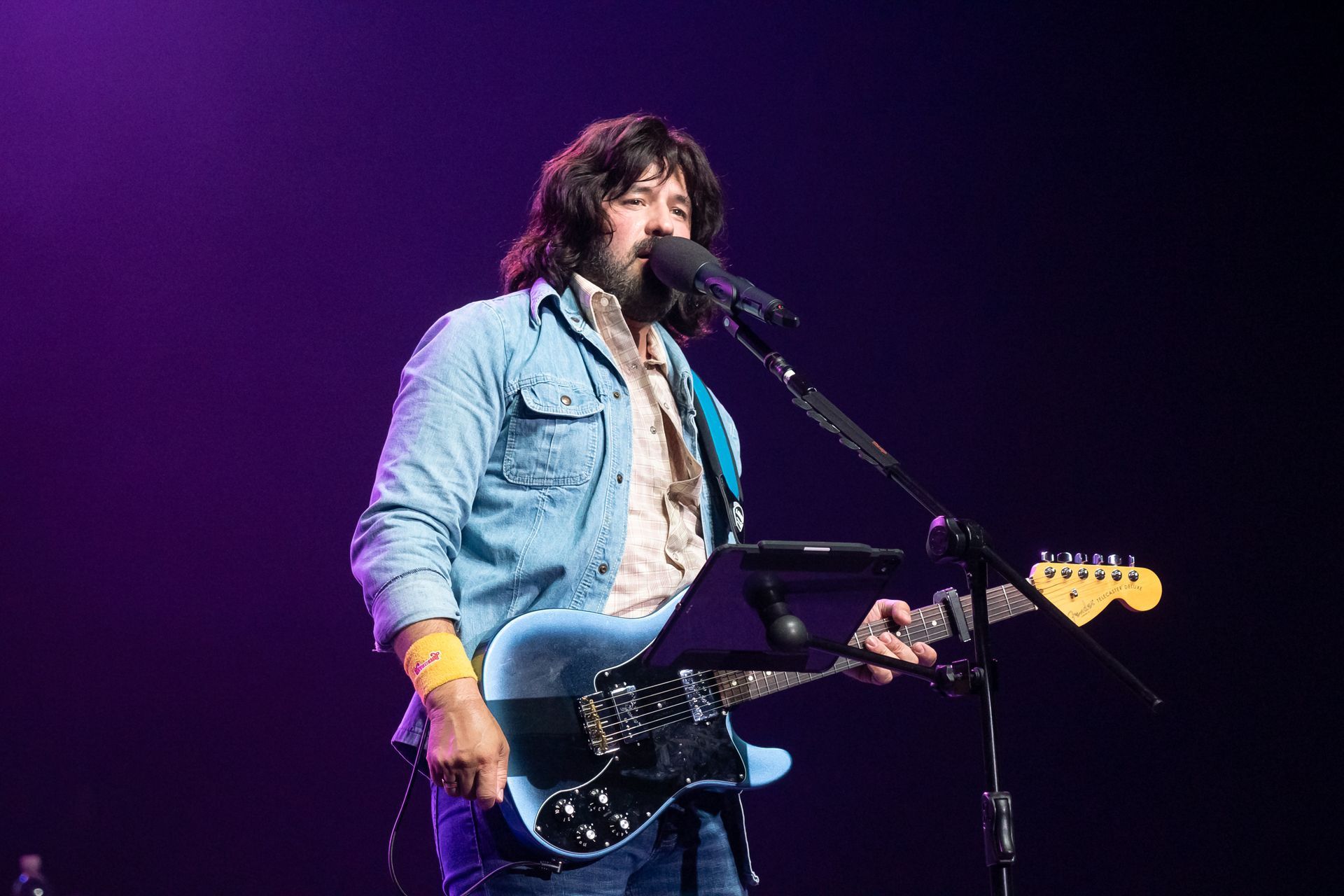 A man is playing a guitar and singing into a microphone on a stage.
