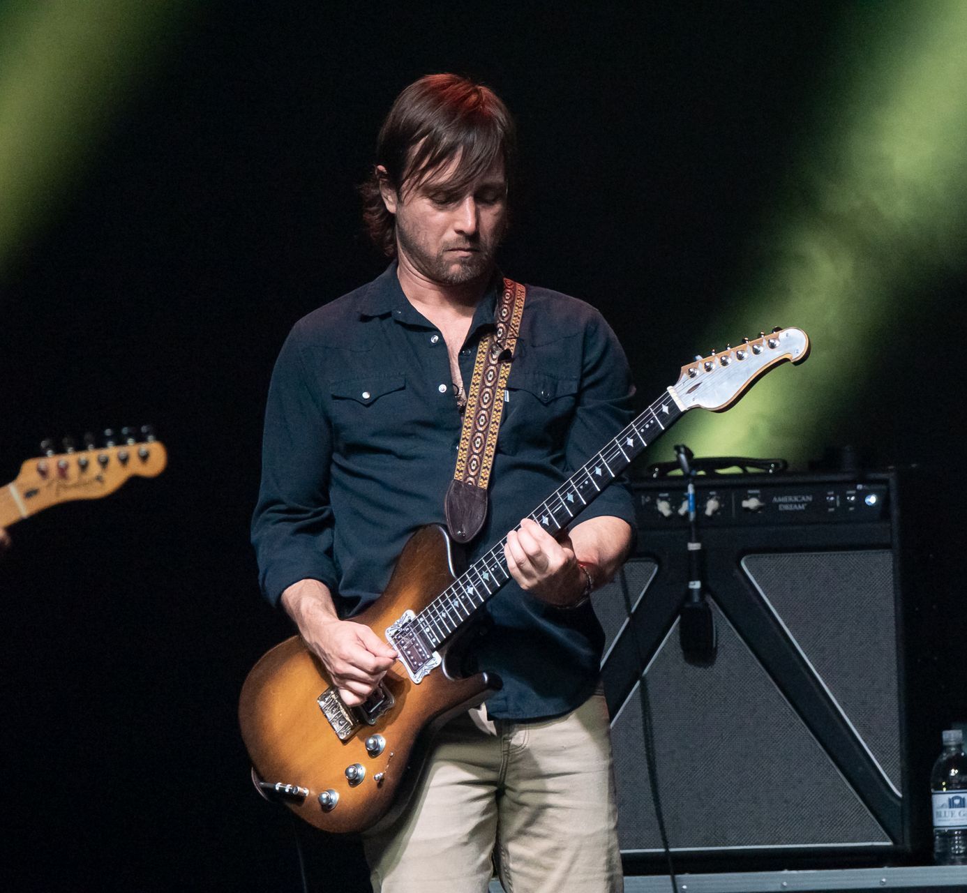 A man playing a guitar on a stage with a bottle of water in the background