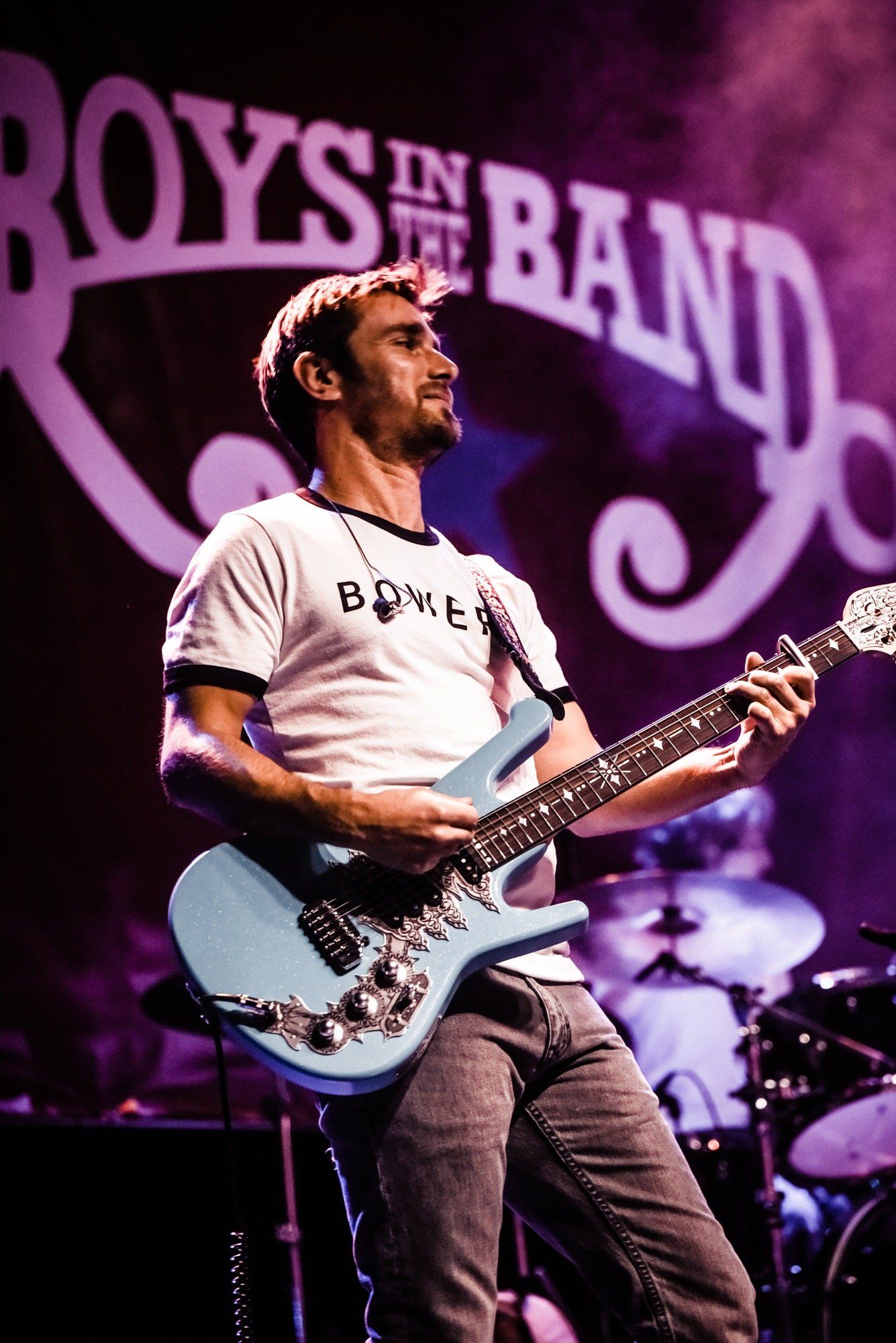 A man is playing a guitar in front of a sign that says boys in the band