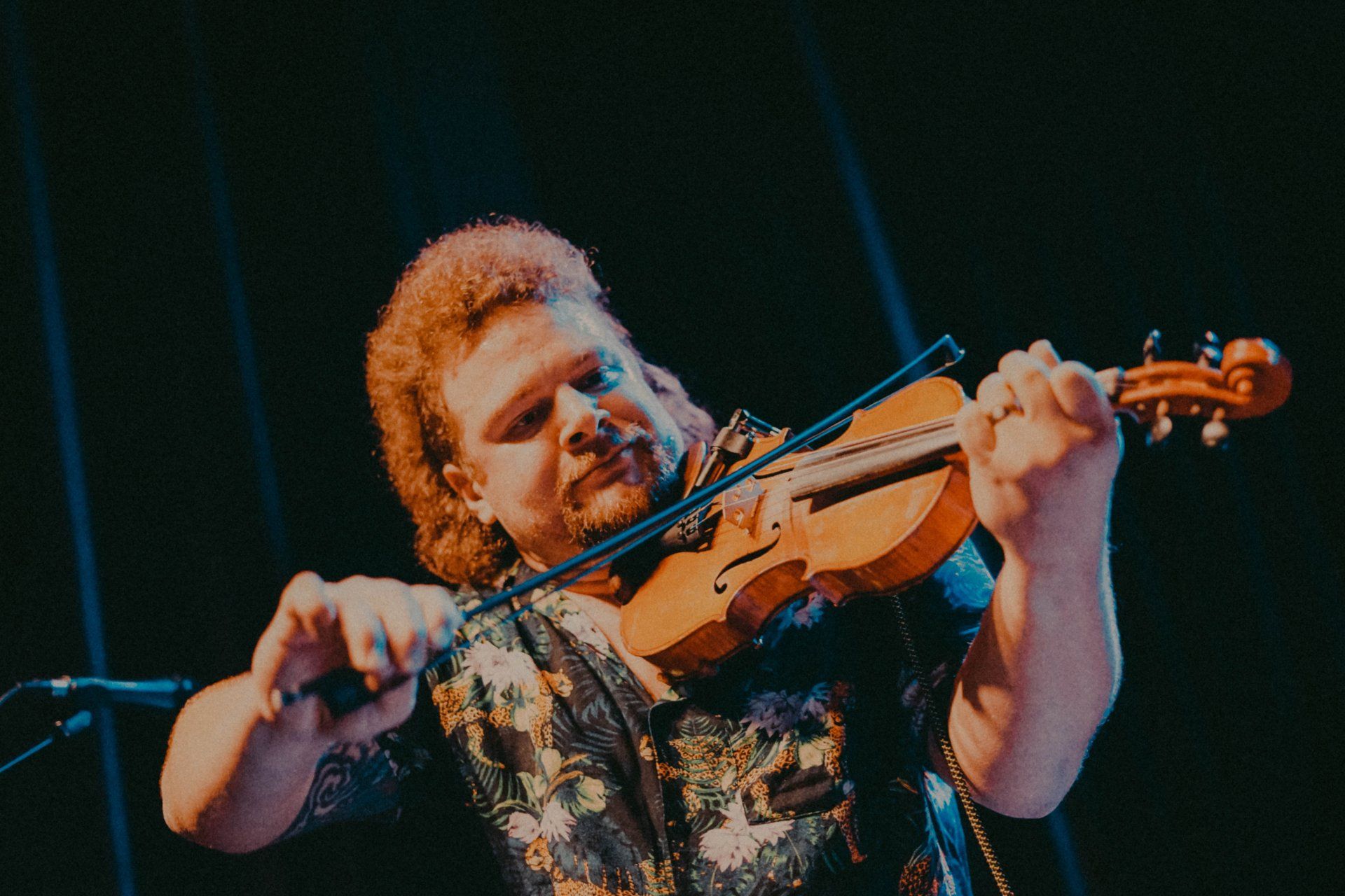 A man is playing a violin on stage in front of a microphone.