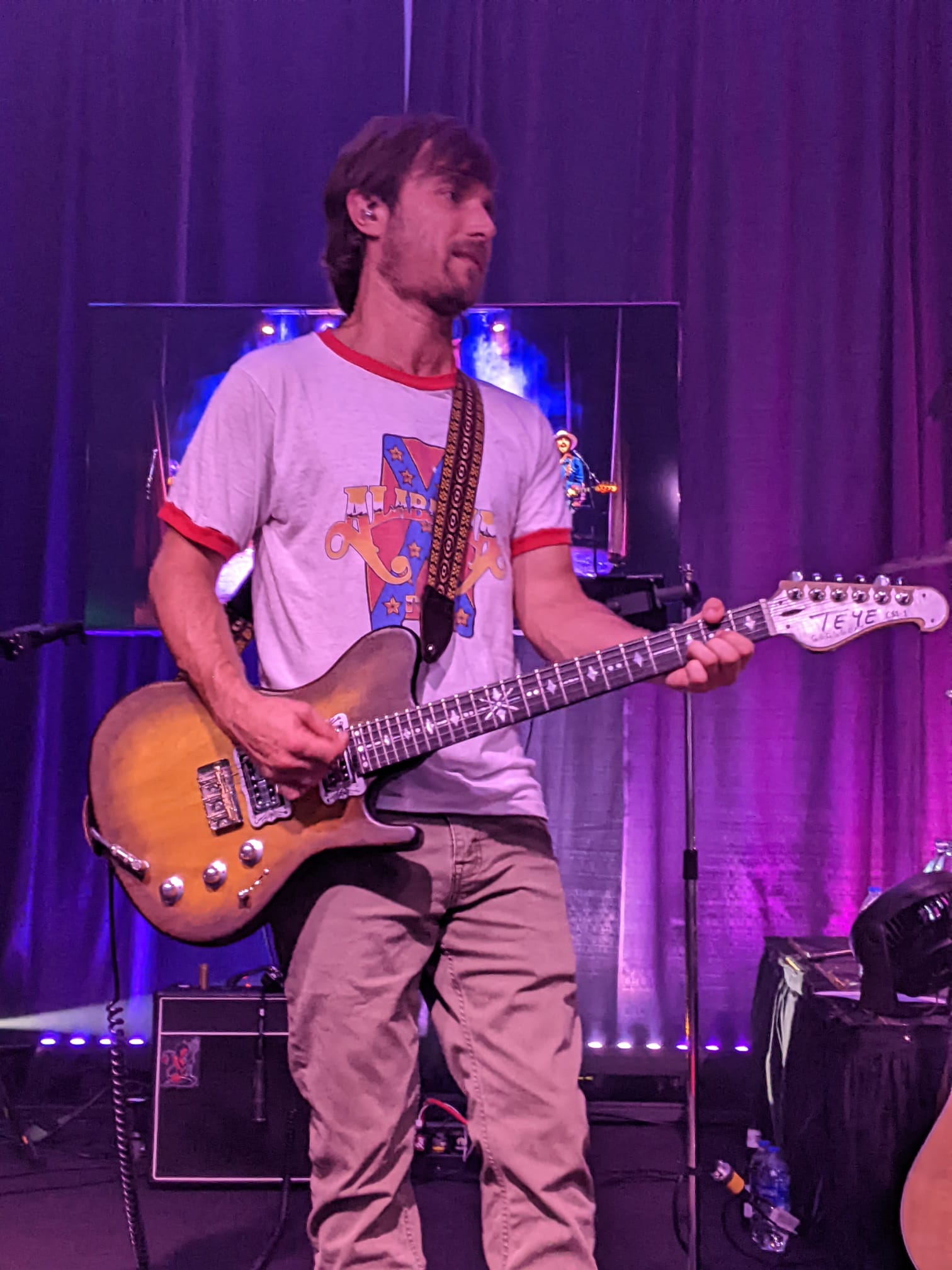 A man is playing a guitar on stage in front of a purple curtain.