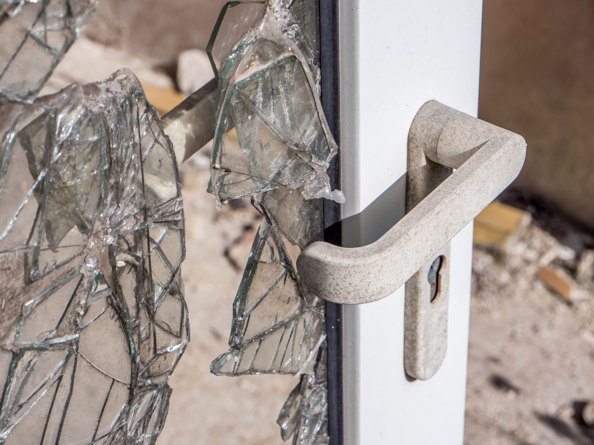 Broken glass in a white door frame with a beige handle.