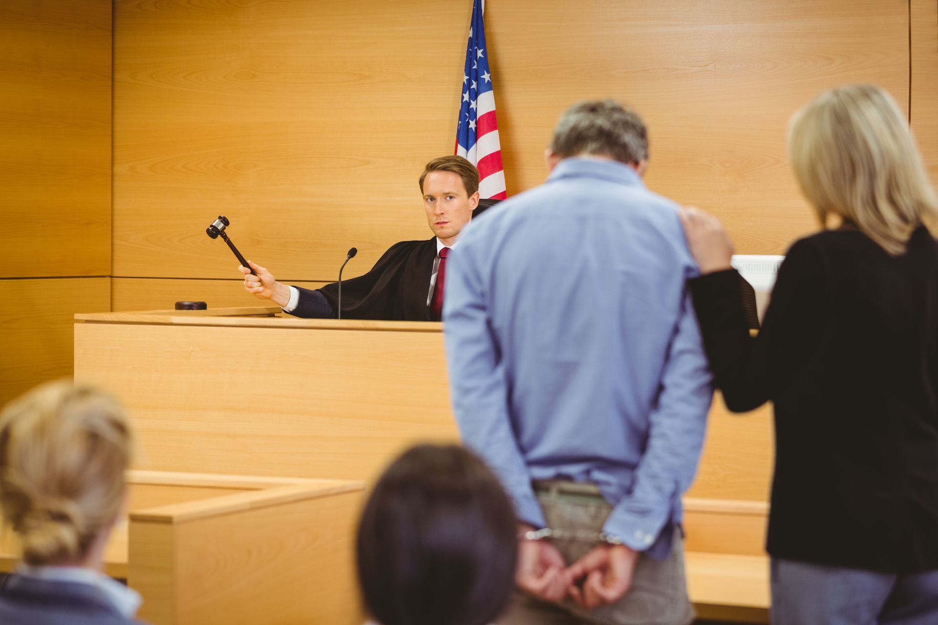 Man in handcuffs with support at a trial, judge with gavel.