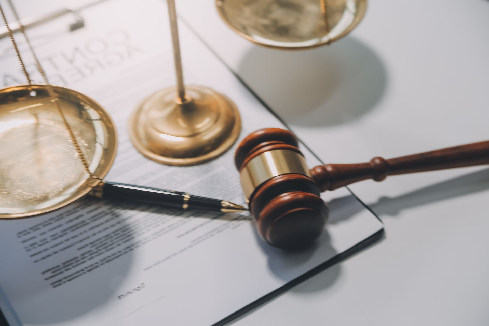 Gavel, scales of justice, and pen on a contract document, symbolizing legal proceedings.