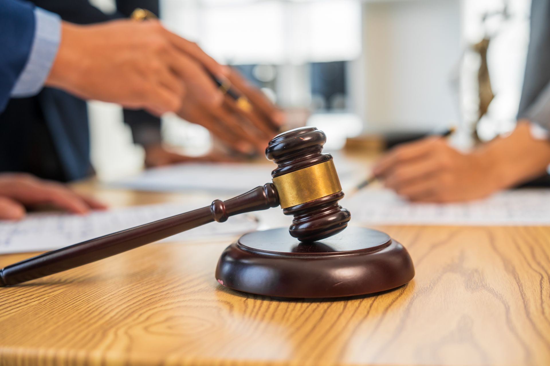 Gavel on wooden surface with blurred hands and documents in background.
