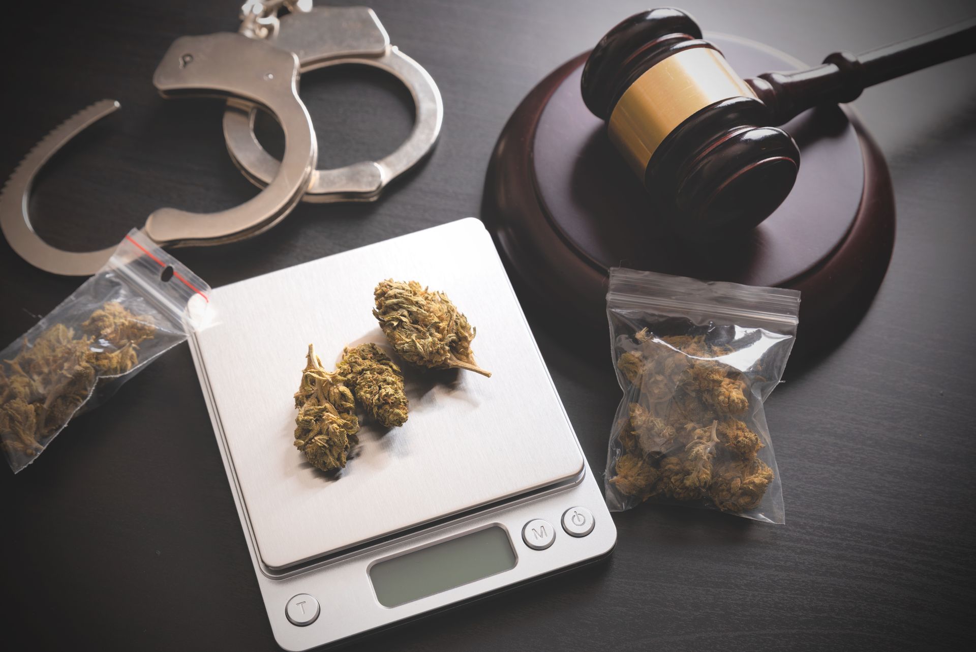 Handcuffs, gavel, and cannabis buds on a scale, suggesting legal implications.