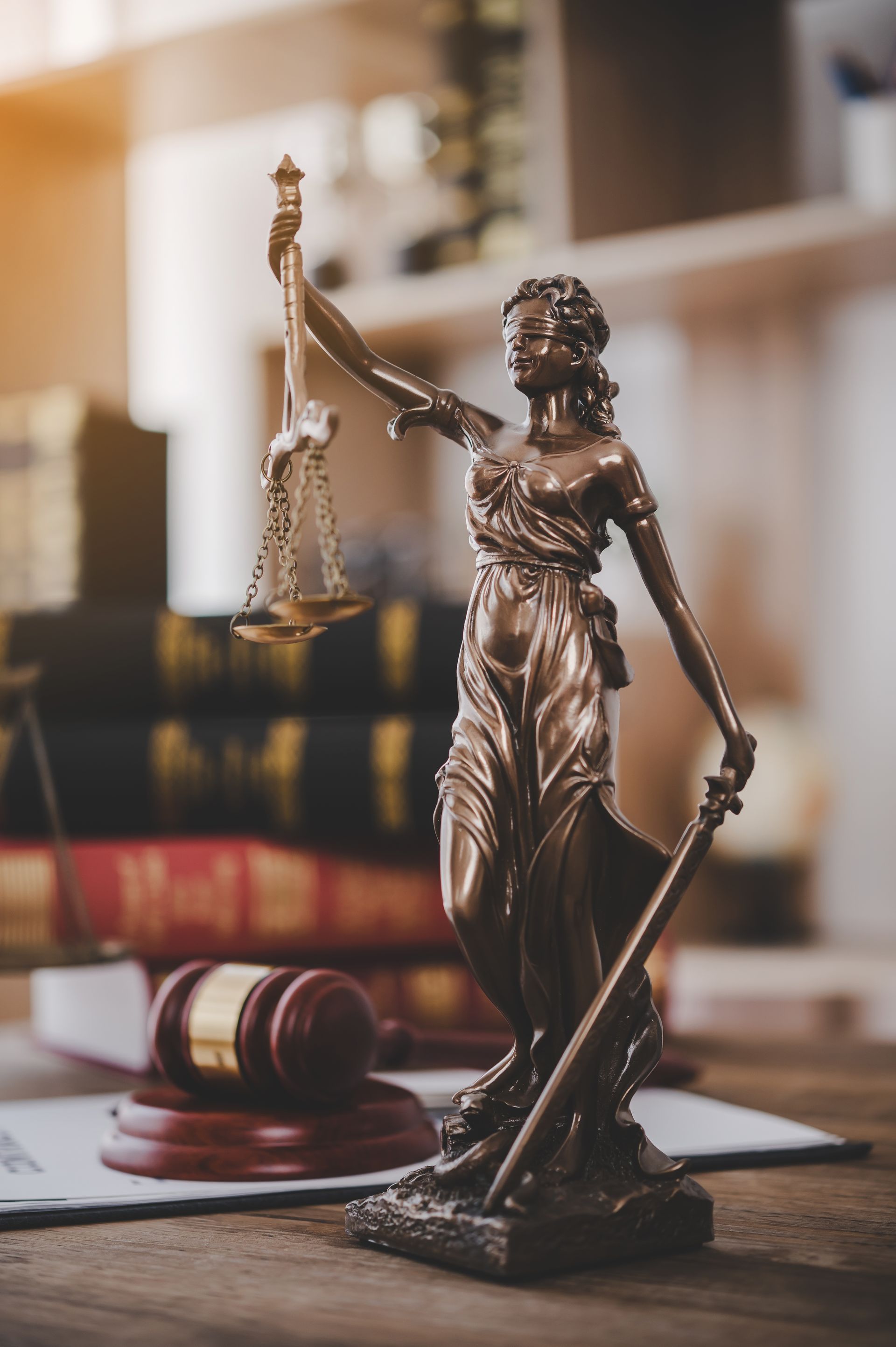 Statue of Lady Justice with scales, a gavel, and legal documents on a wooden desk.