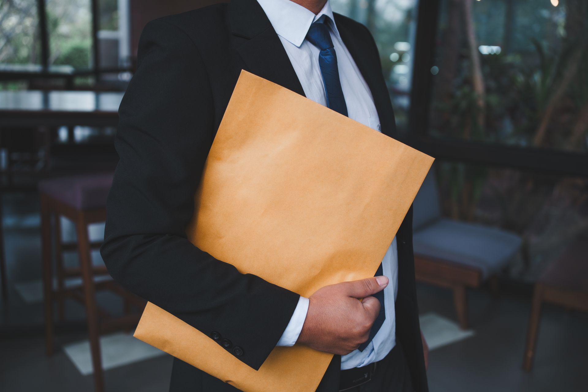 Person in a suit holds a large brown envelope; inside office setting.