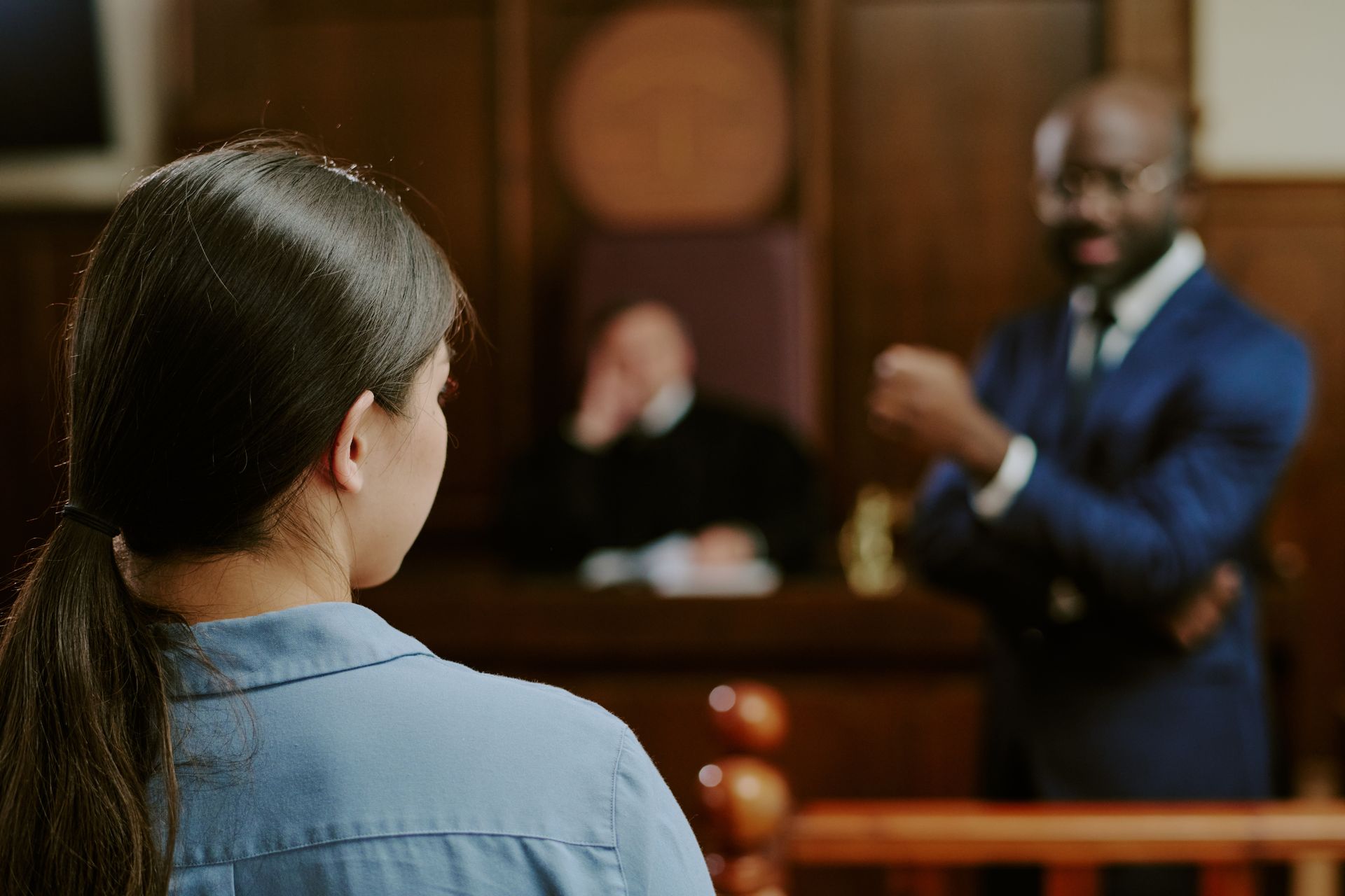 Woman in courtroom facing a lawyer, with judge seated in background.