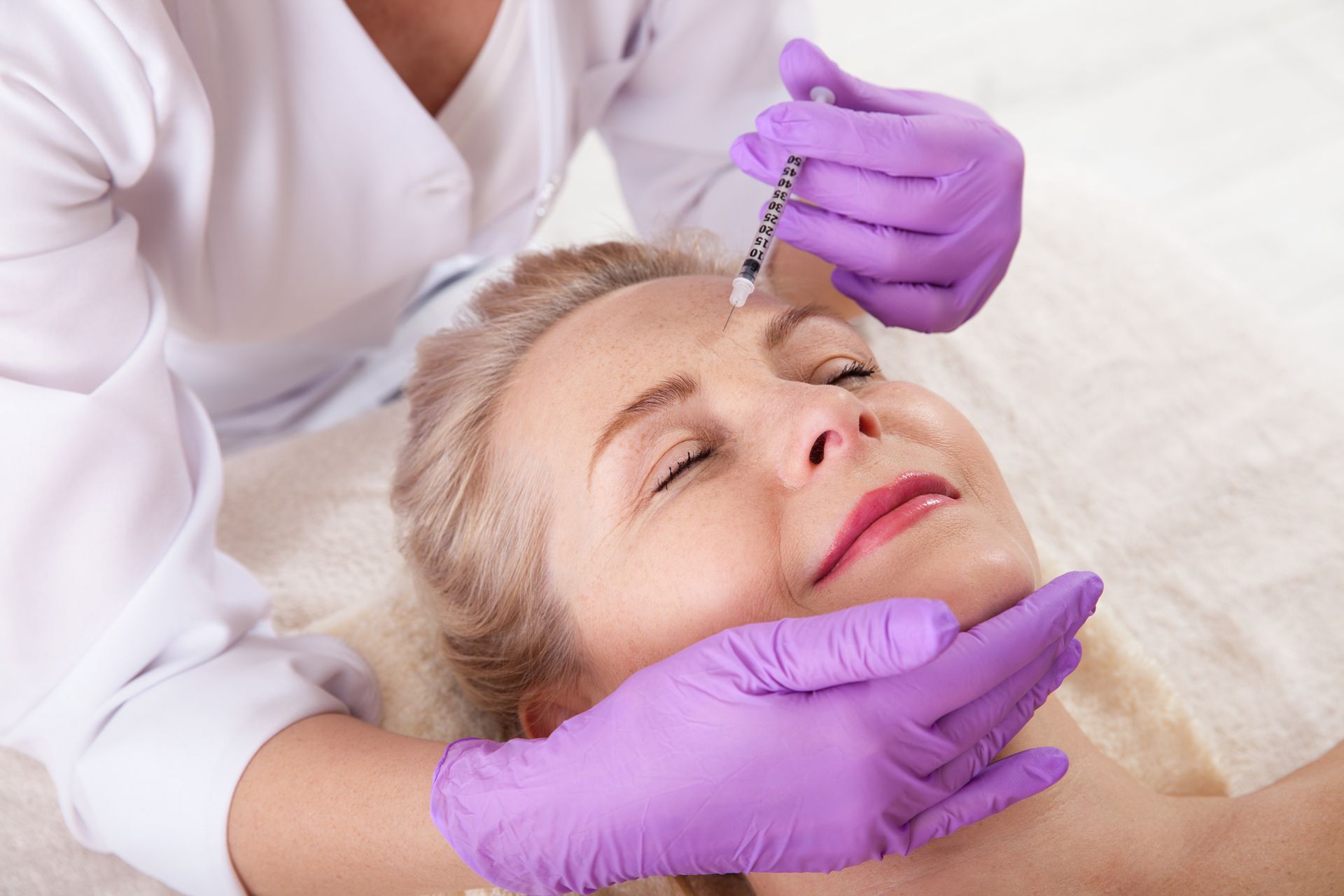 Woman receiving facial injections from a person wearing purple gloves.