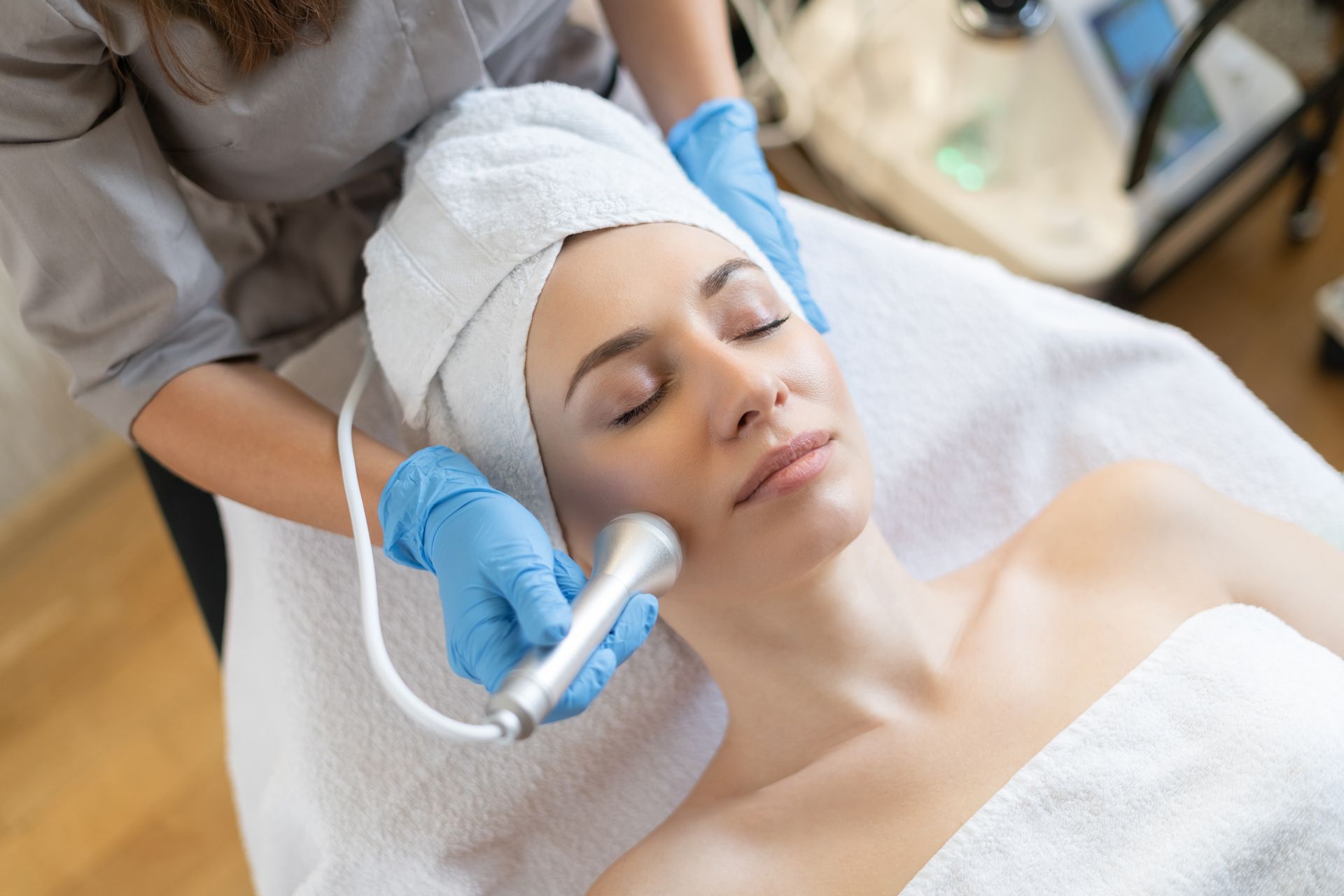 Woman receiving facial treatment in a spa, therapist holding a device over her face.