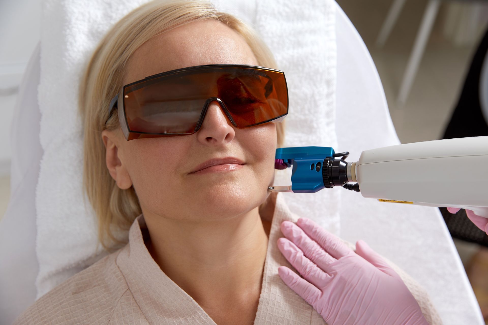 Woman receiving facial laser treatment, wearing protective eyewear.