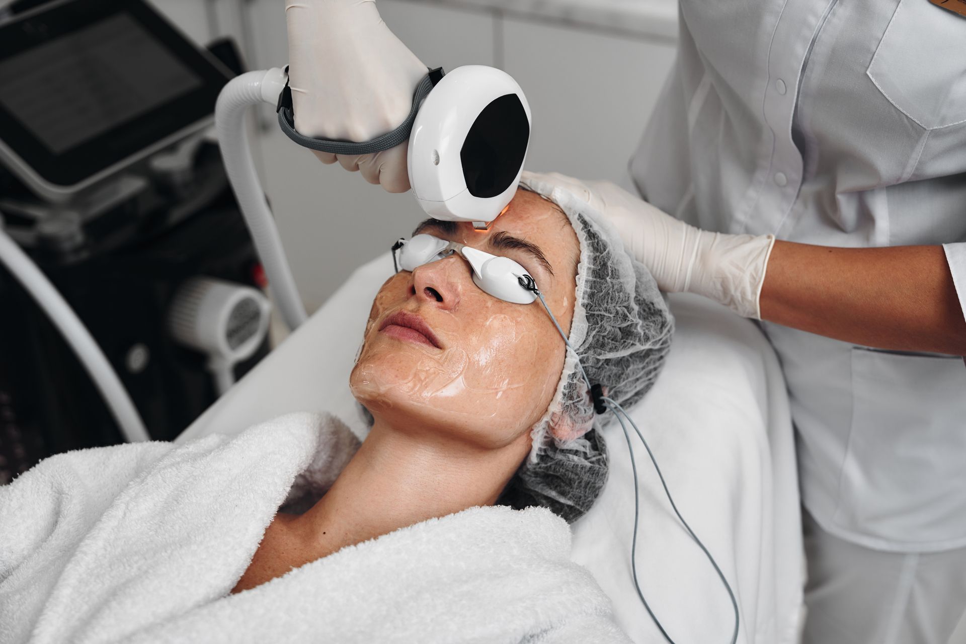 Cosmetic facial treatment with a handheld device applied to a client wearing eye pads and a towel wrap