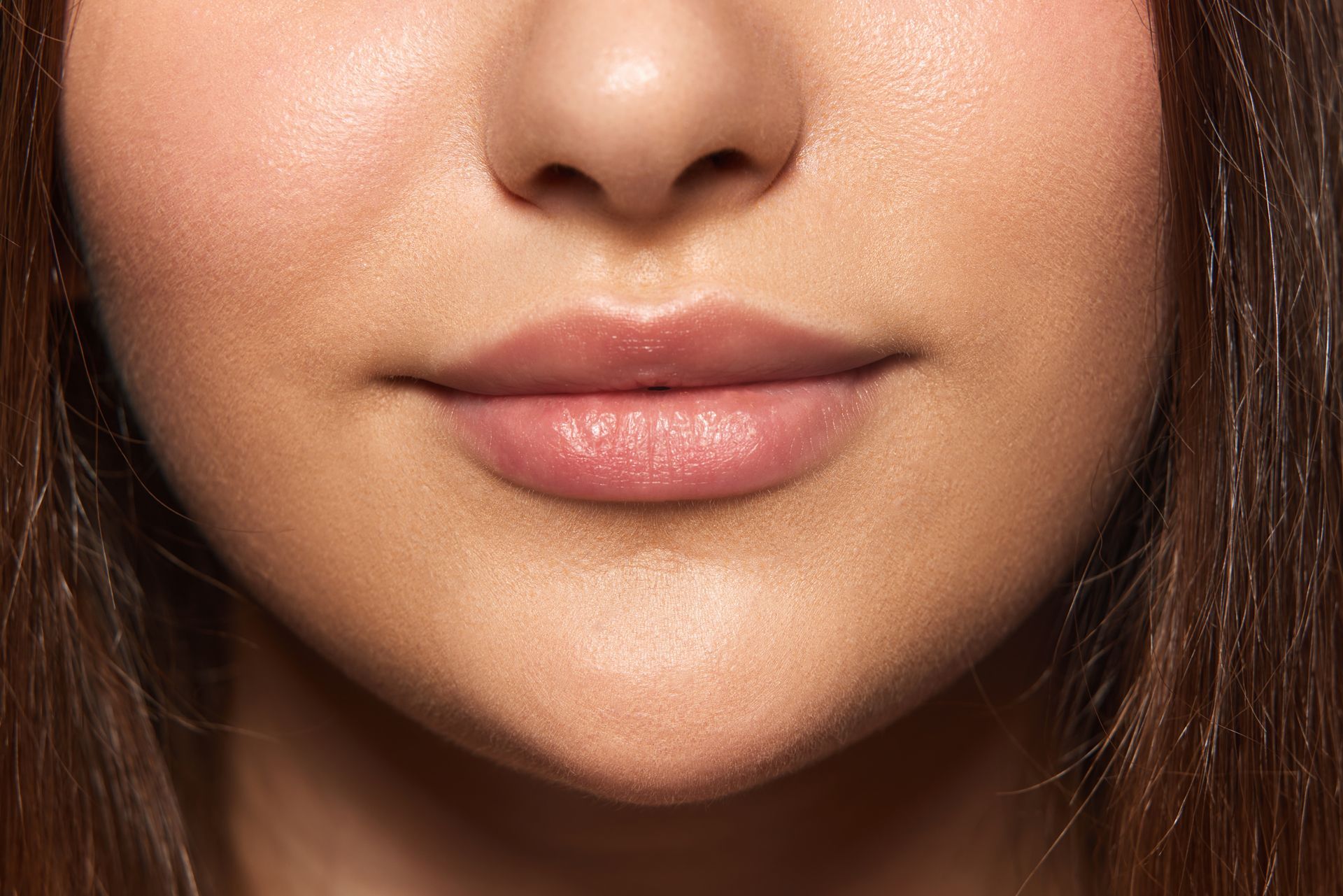 Close-up of a person's lips and nose; the lips are a light pink and skin is slightly shiny.