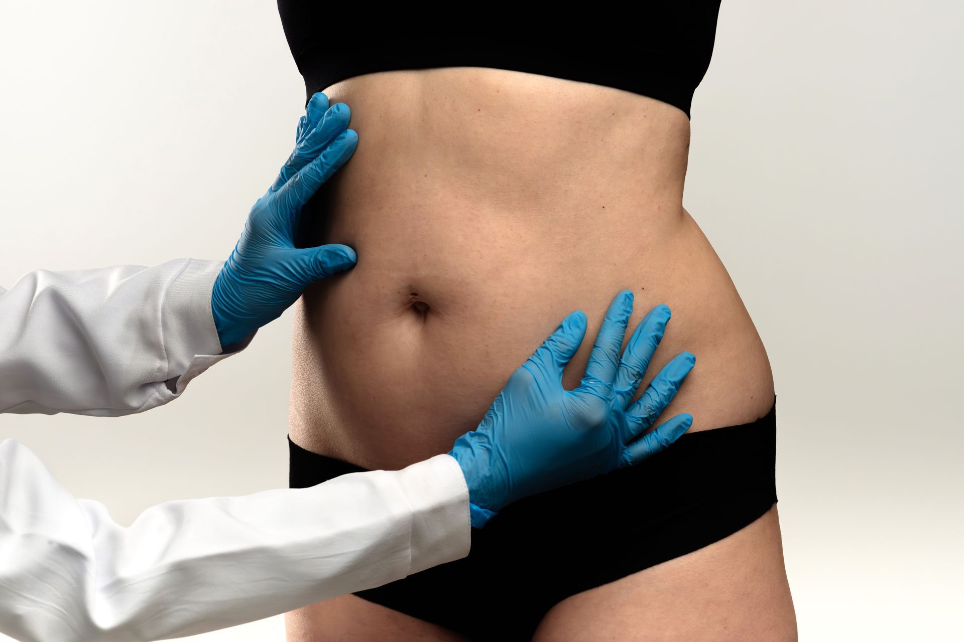 A person's abdomen is being examined by a doctor wearing blue gloves and a white coat.