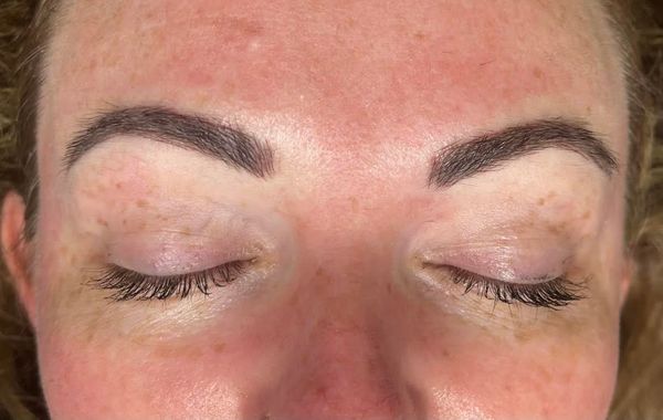 Close-up of a person's closed eyes, dark eyebrows, and visible freckles on the face.