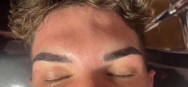 Close-up of a person's closed eyes and newly done eyebrow tattoo.