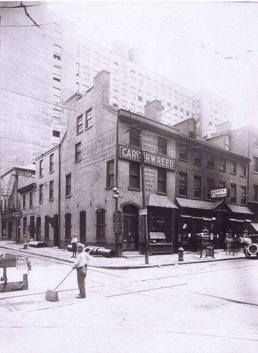 A man is sweeping the street in front of a building that has the word tavern on it