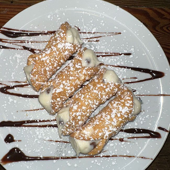 a white plate topped with cannoli with chocolate sauce and powdered sugar