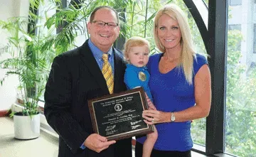 A man in a suit and tie is holding a child and a plaque.