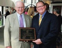 Two men in suits and ties are standing next to each other holding a plaque.
