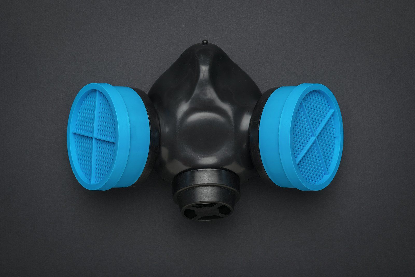 A gas mask with two blue filters on a black surface.