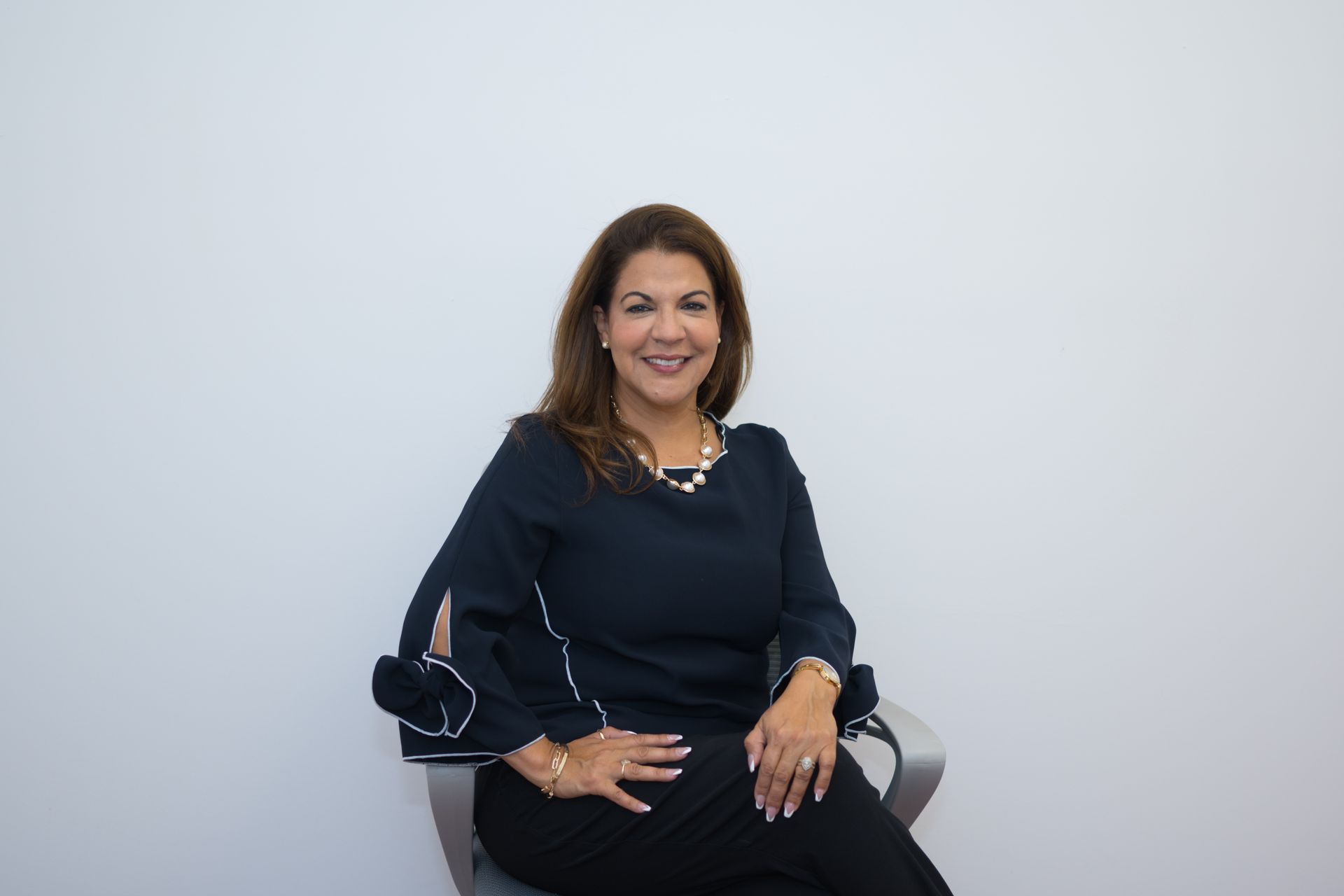 A woman is sitting in a chair with her hands on her knees and smiling.