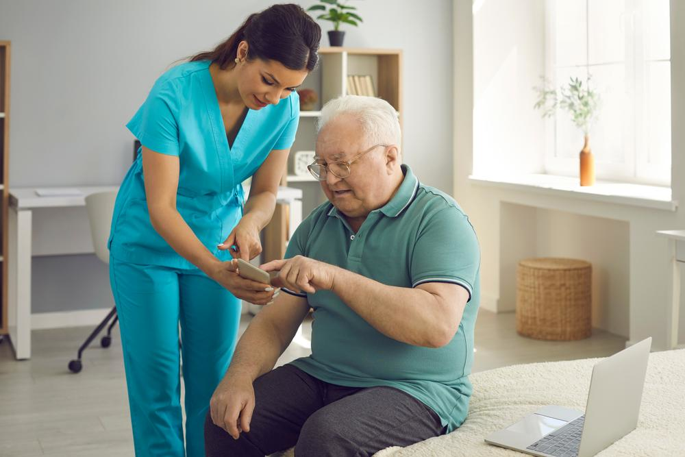 A nurse is helping an elderly man use a cell phone.
