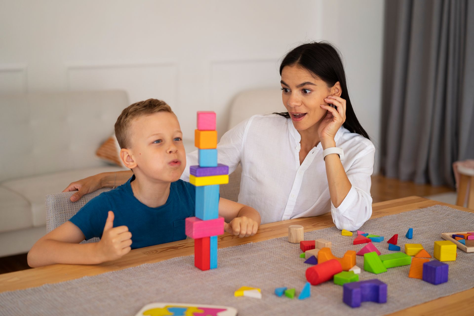 A woman and a boy are playing with wooden blocks at a table.