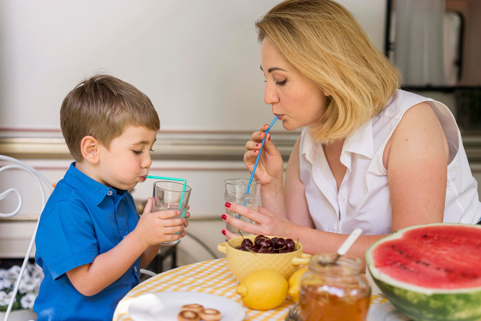 A woman and a child are drinking water through straws at a table.