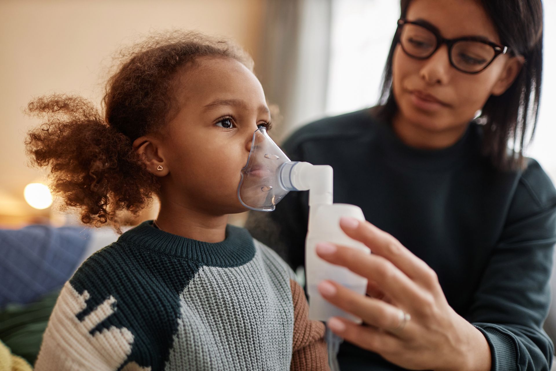 A woman is giving a little girl an inhaler.