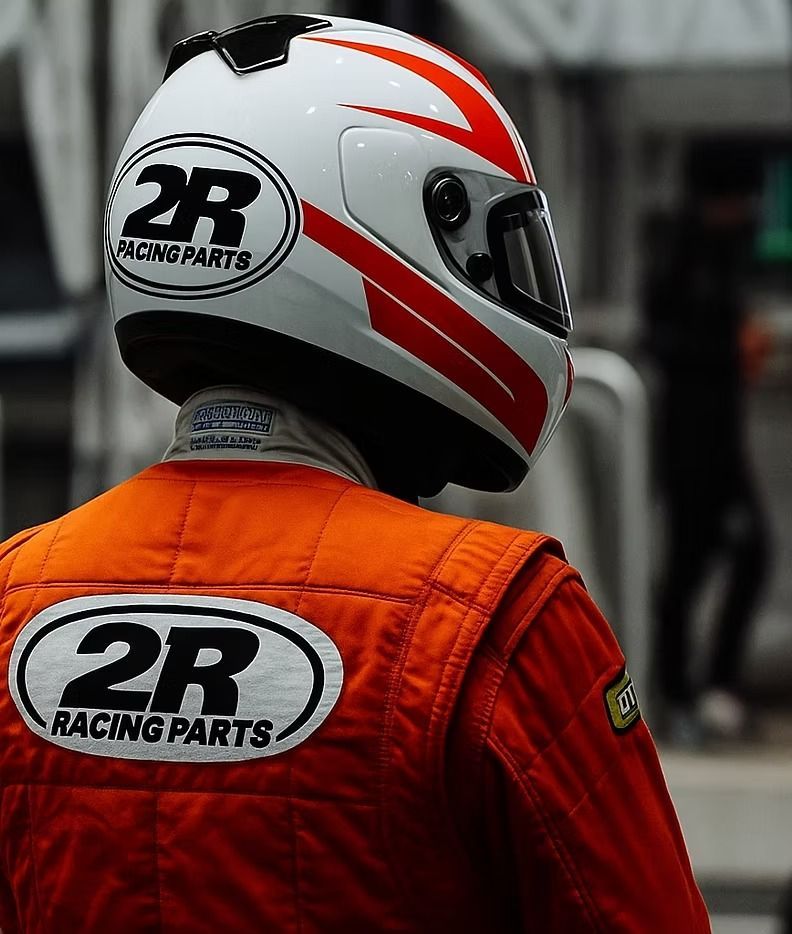 Piloto de carreras con traje naranja y casco blanco con el logotipo de 2R Racing Parts, visto desde atrás.