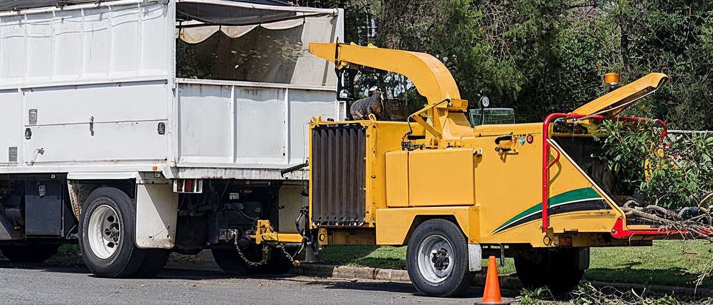 A yellow wood chipper connected to a white truck is processing branches.