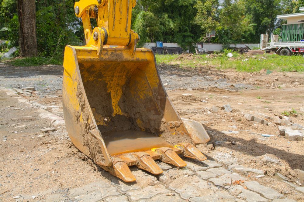 Yellow excavator bucket on dirt and paving stones.