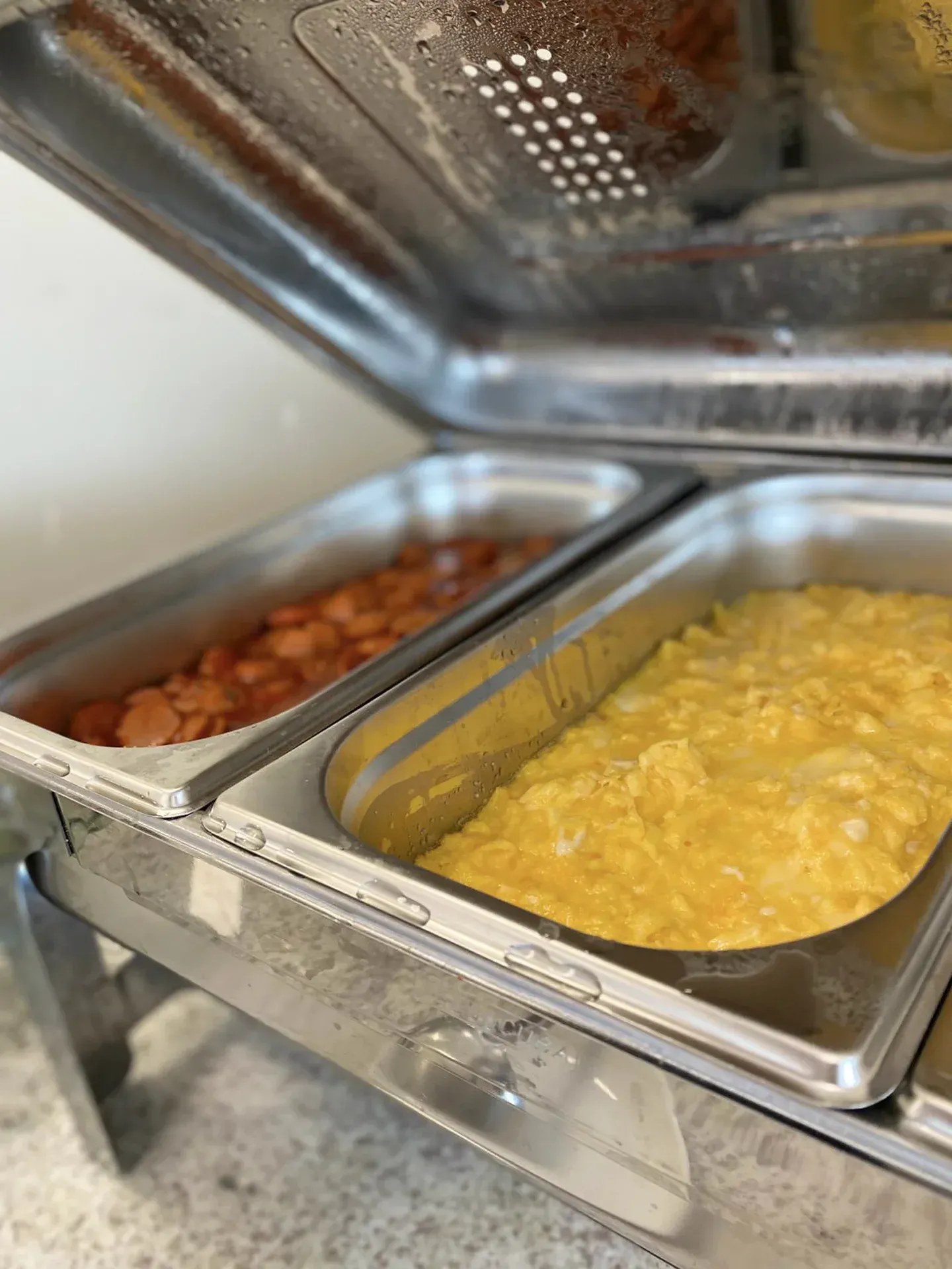 Um aquecedor de buffet prateado com ovos mexidos e linguiça em panelas de metal.