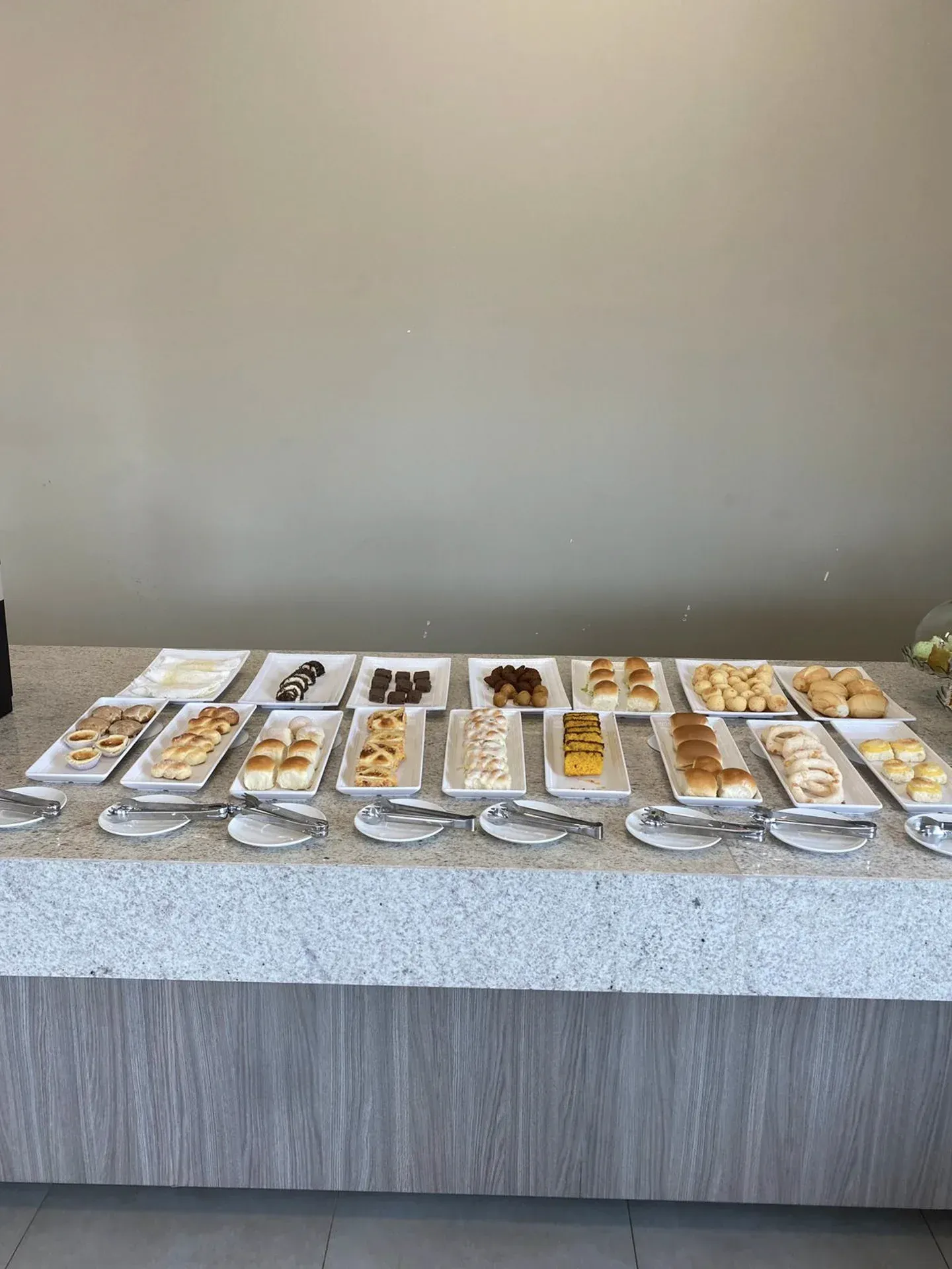 Um bufê de sobremesas com diversos doces em pratos brancos, pinças de prata e uma bancada de granito.