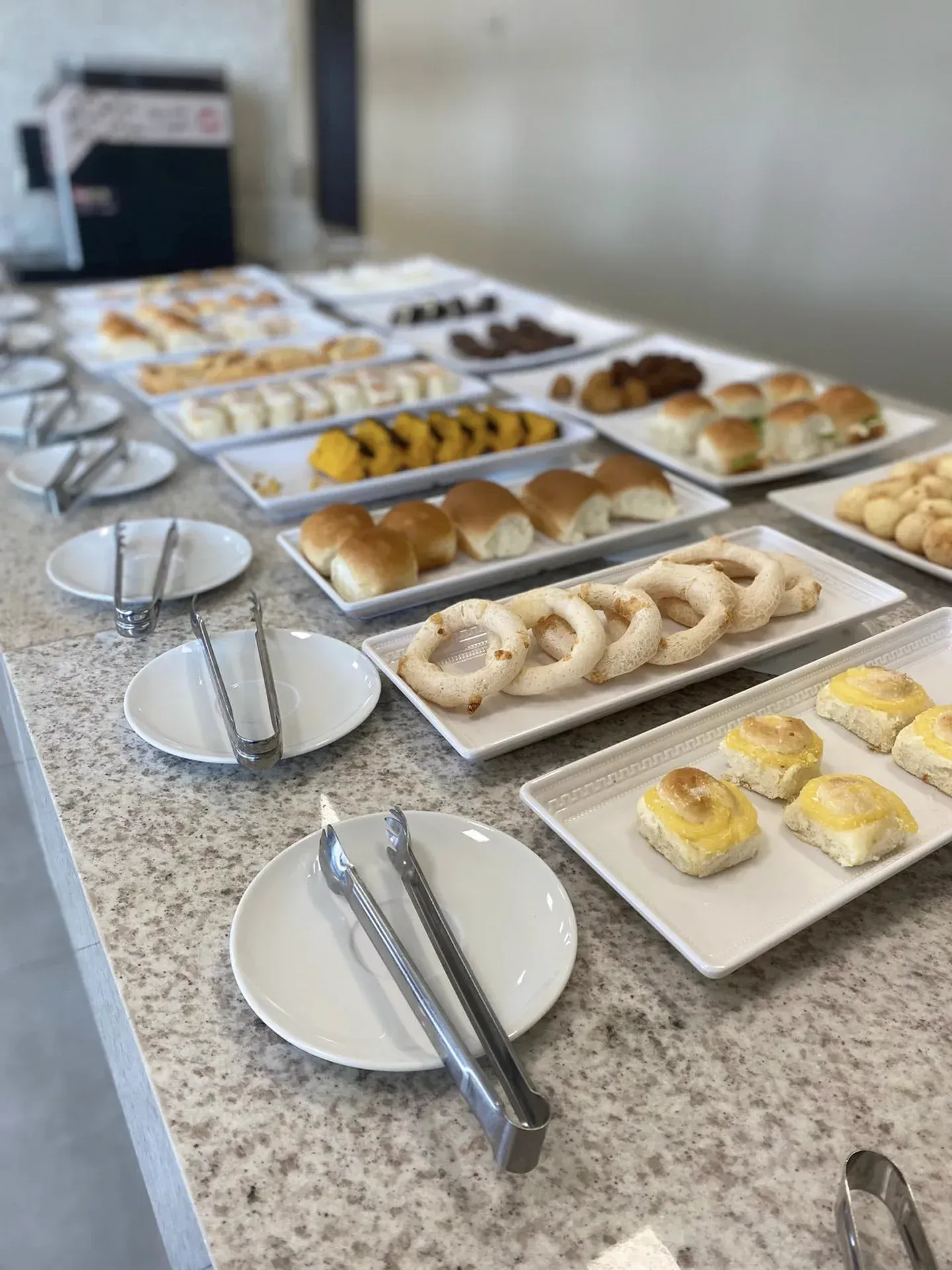 Mesa de bufê com diversos doces e pães em travessas brancas.