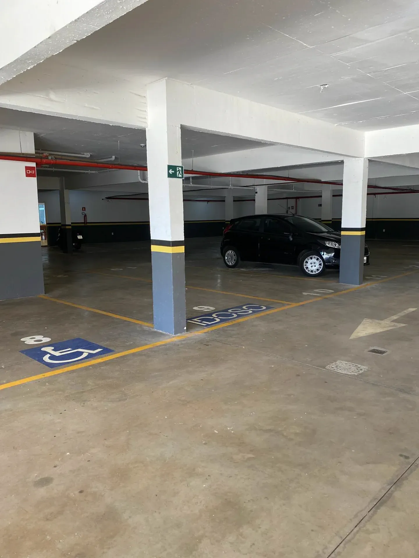 Uma garagem coberta vazia com um carro preto. Vaga reservada para deficientes físicos.