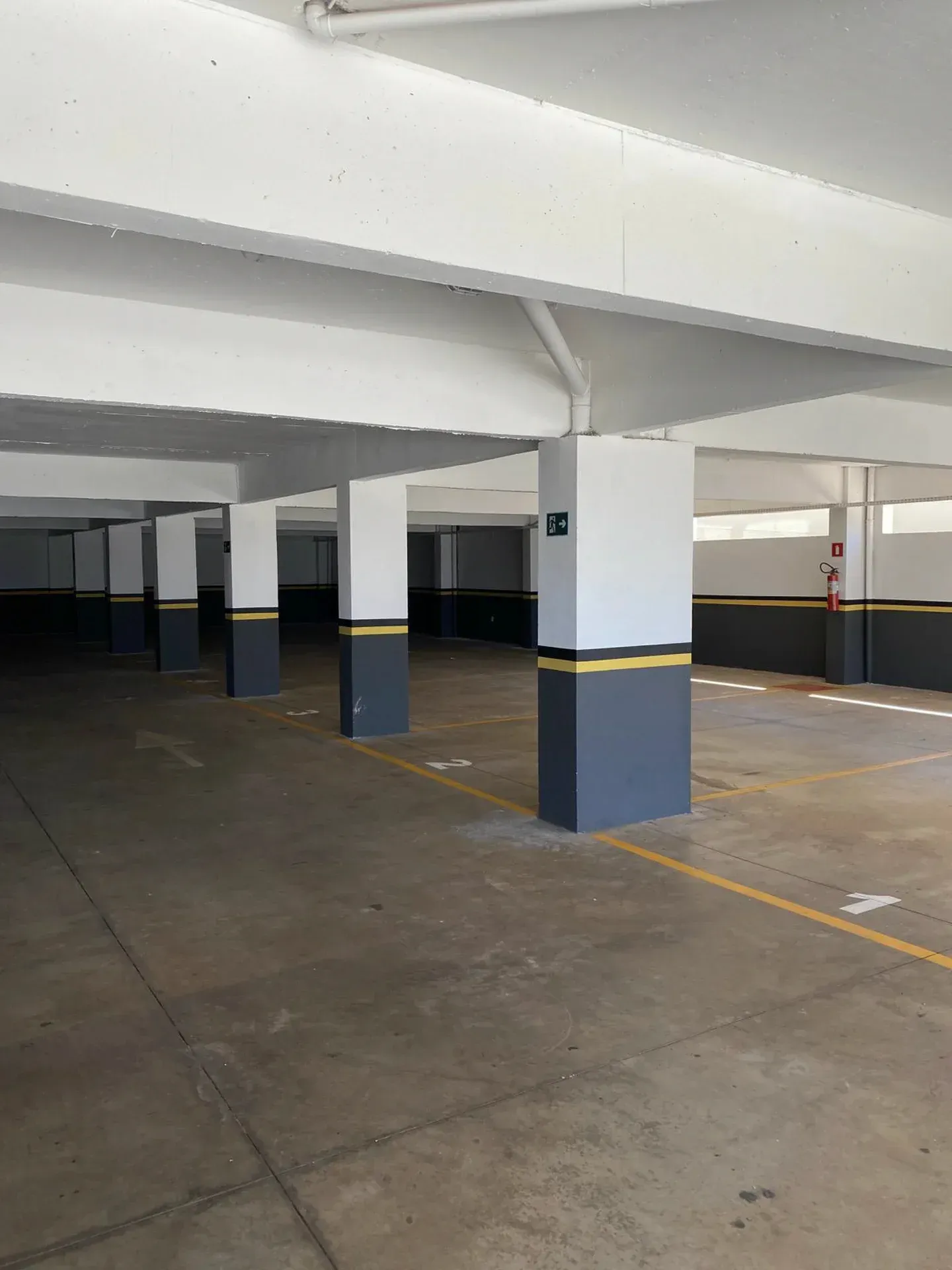 Garagem de estacionamento vazia com colunas cinza, pretas e amarelas e piso de concreto.