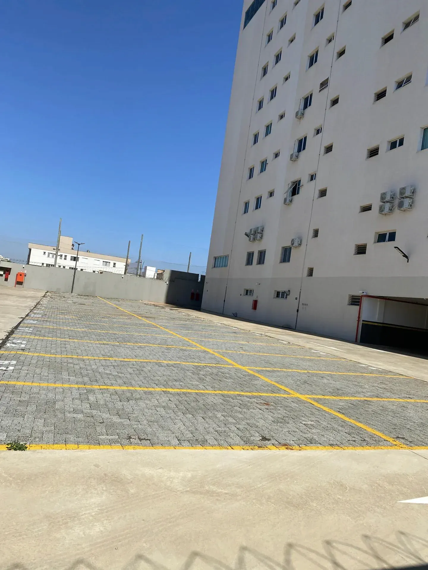 Estacionamento vazio ao lado de um prédio alto e branco sob um céu azul claro.