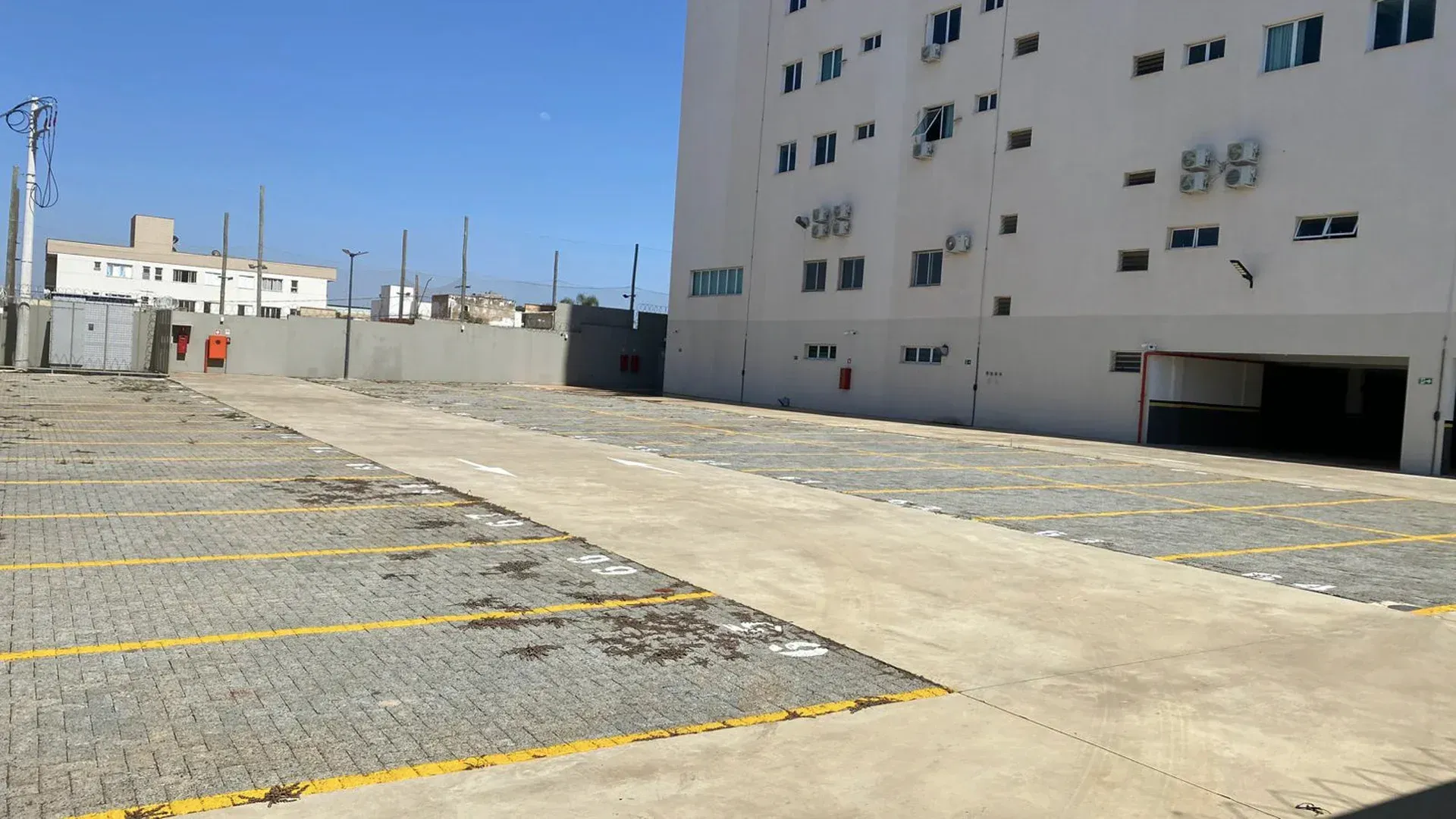 Estacionamento vazio ao lado de um prédio branco sob um céu azul claro.