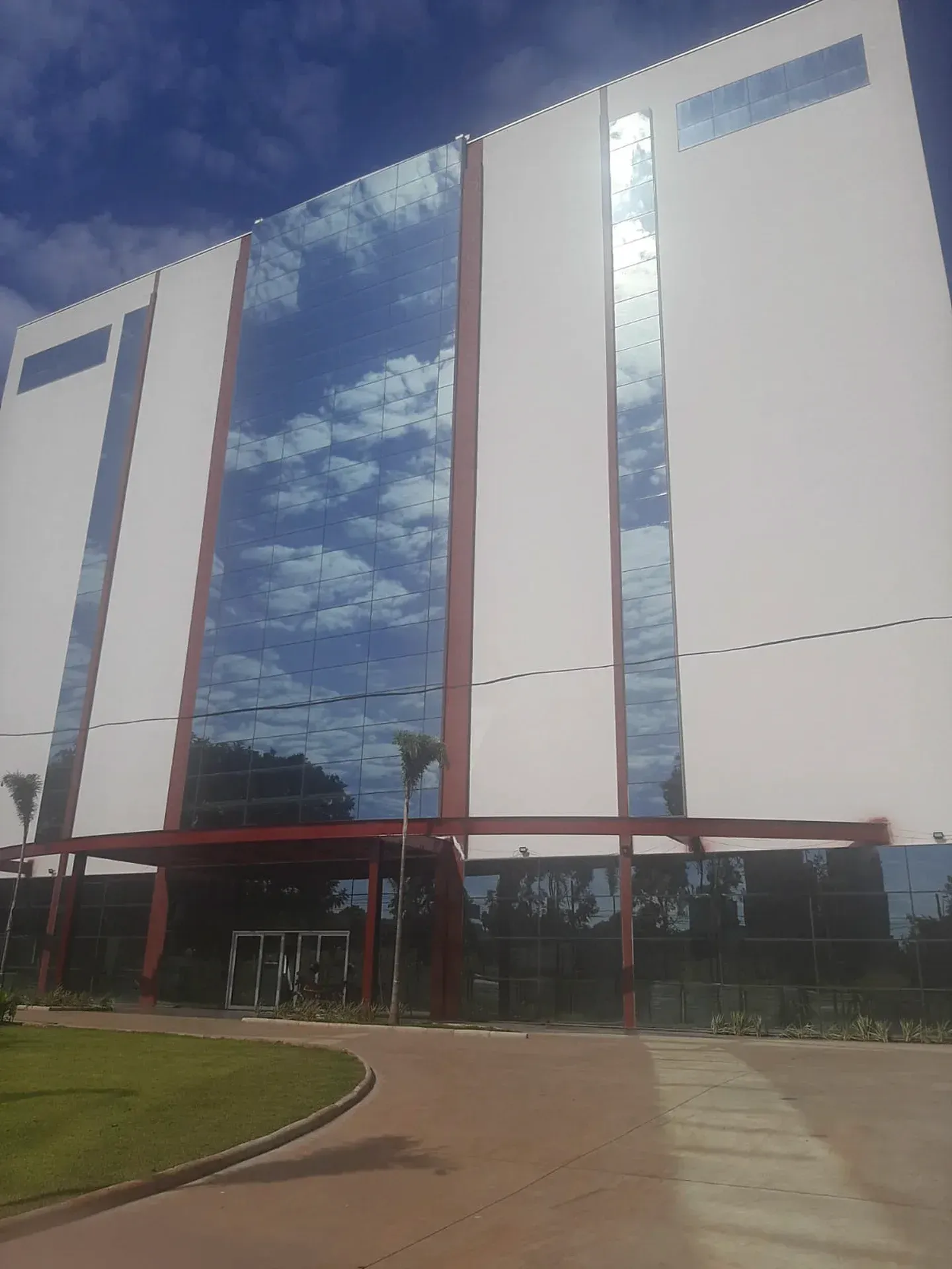 Prédio moderno branco com painéis de vidro que refletem um céu azul nublado.