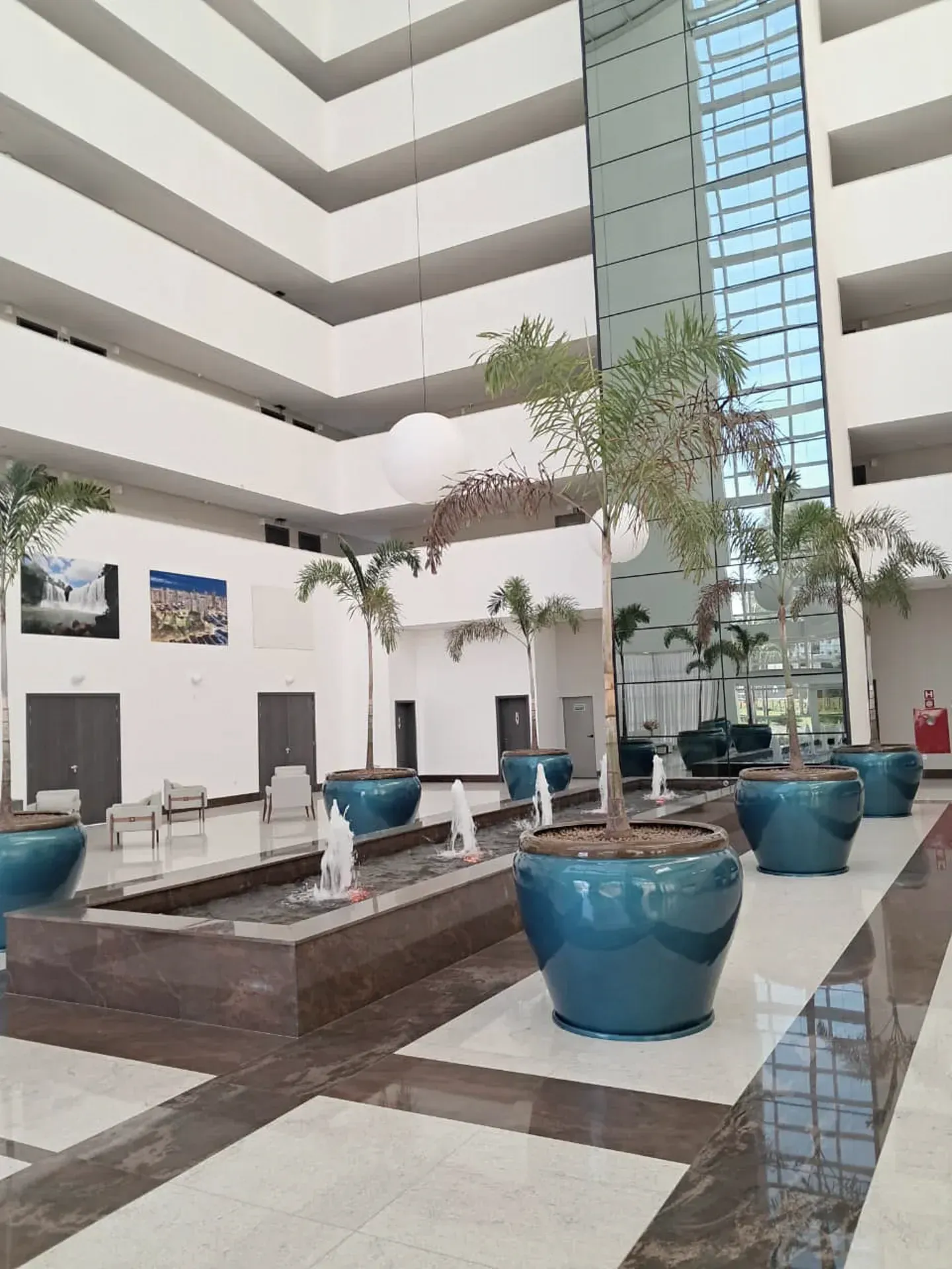 Vista interior de um edifício moderno com árvores em vasos, fontes de água e um átrio de vários andares.