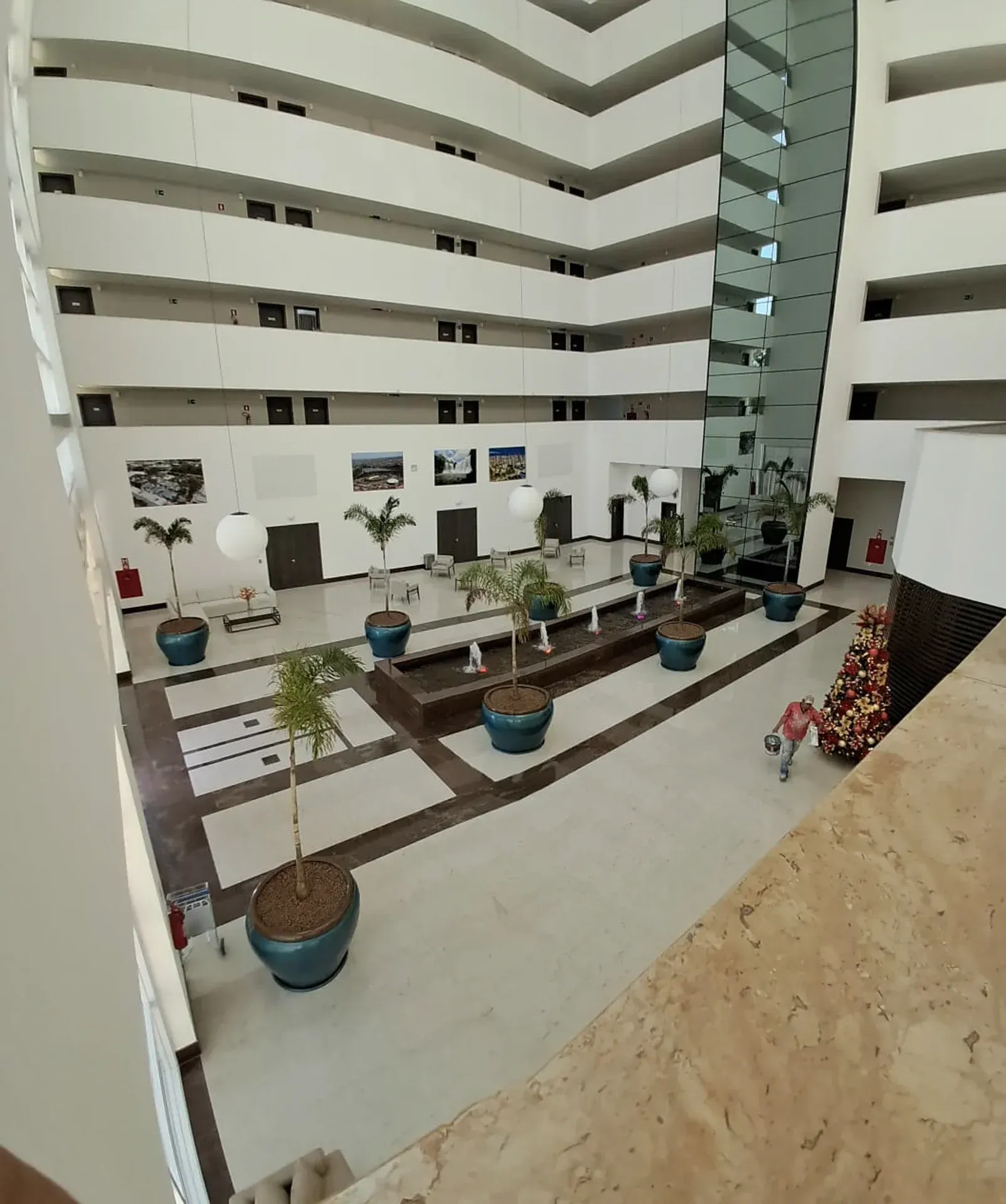 Grande átrio aberto de vários andares com piso de azulejos e plantas em vasos. Os andares do edifício são visíveis.