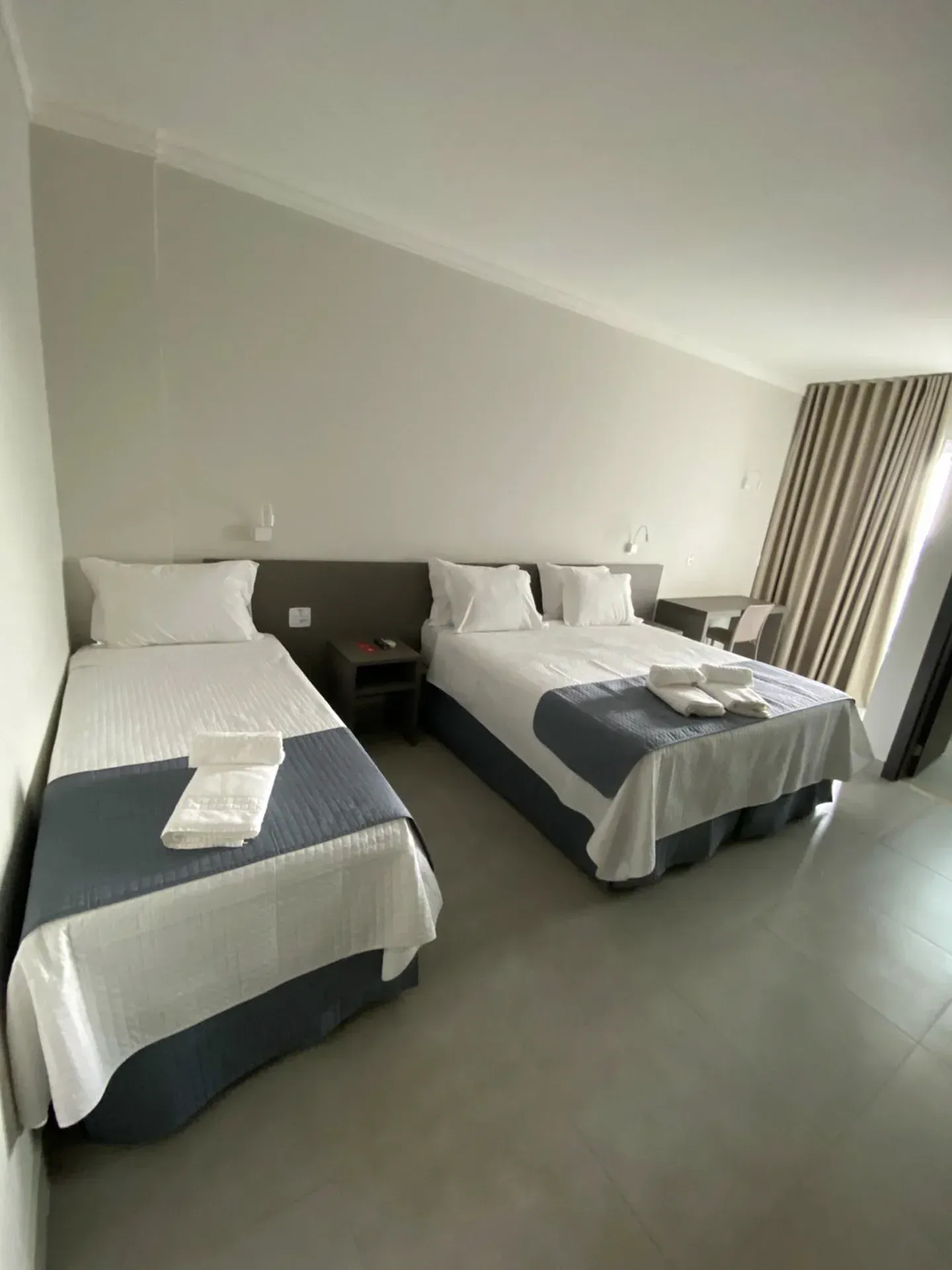 Duas camas com lençóis brancos e colchas azuis em um quarto de cores claras.