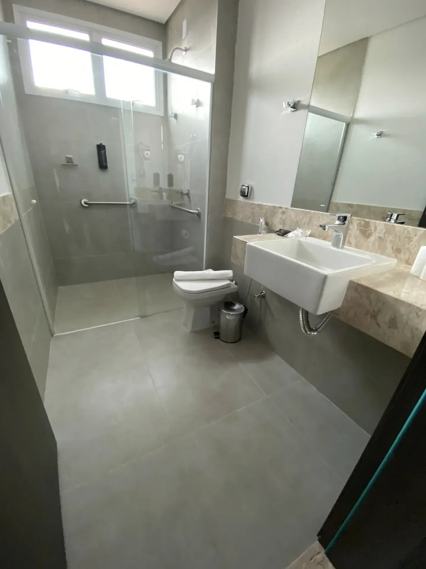 Banheiro com piso de azulejo cinza, pia branca e box de vidro.