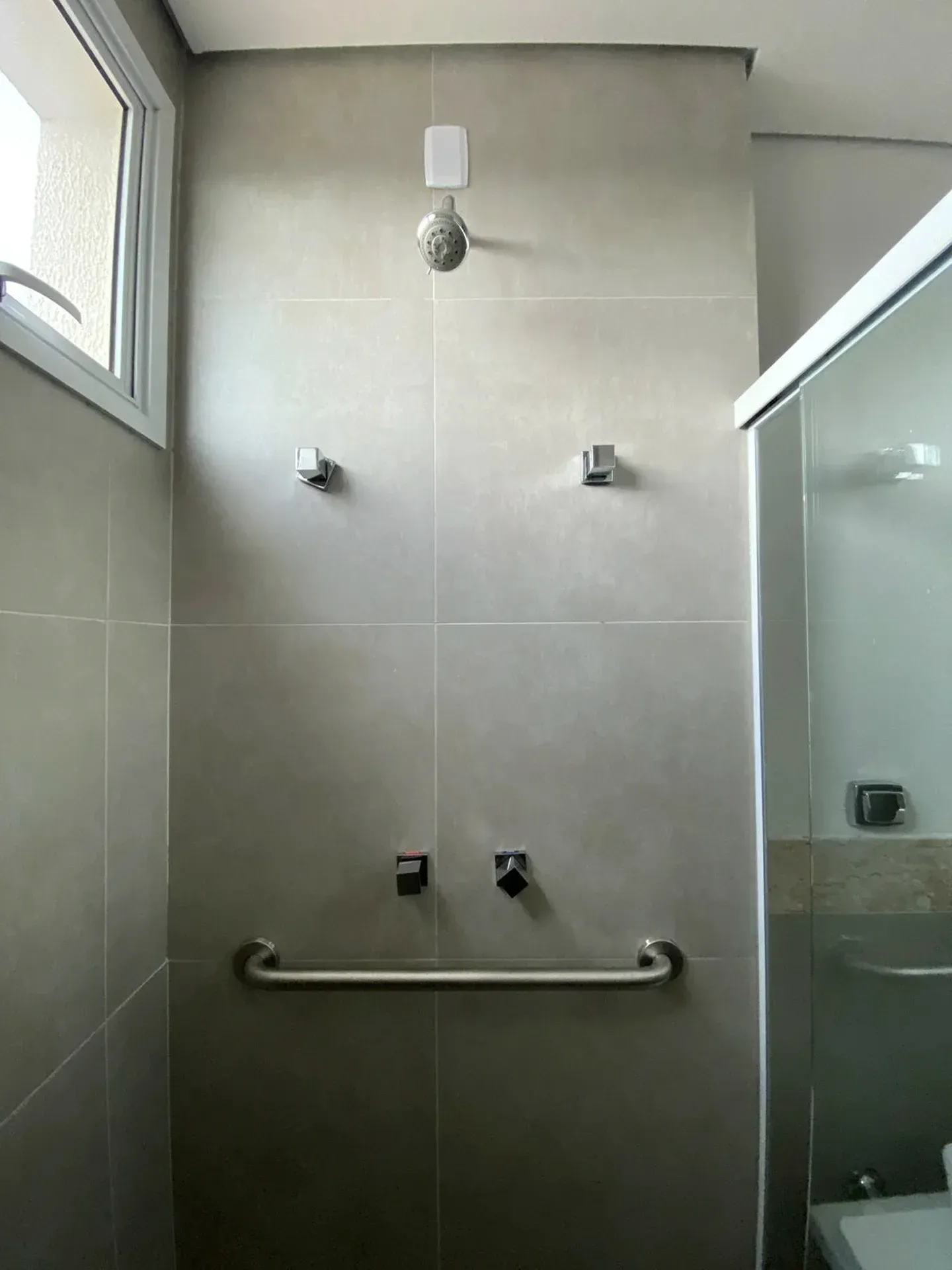 Box de chuveiro com paredes revestidas de azulejos cinza, chuveiro de mão, barra de apoio e acessórios.