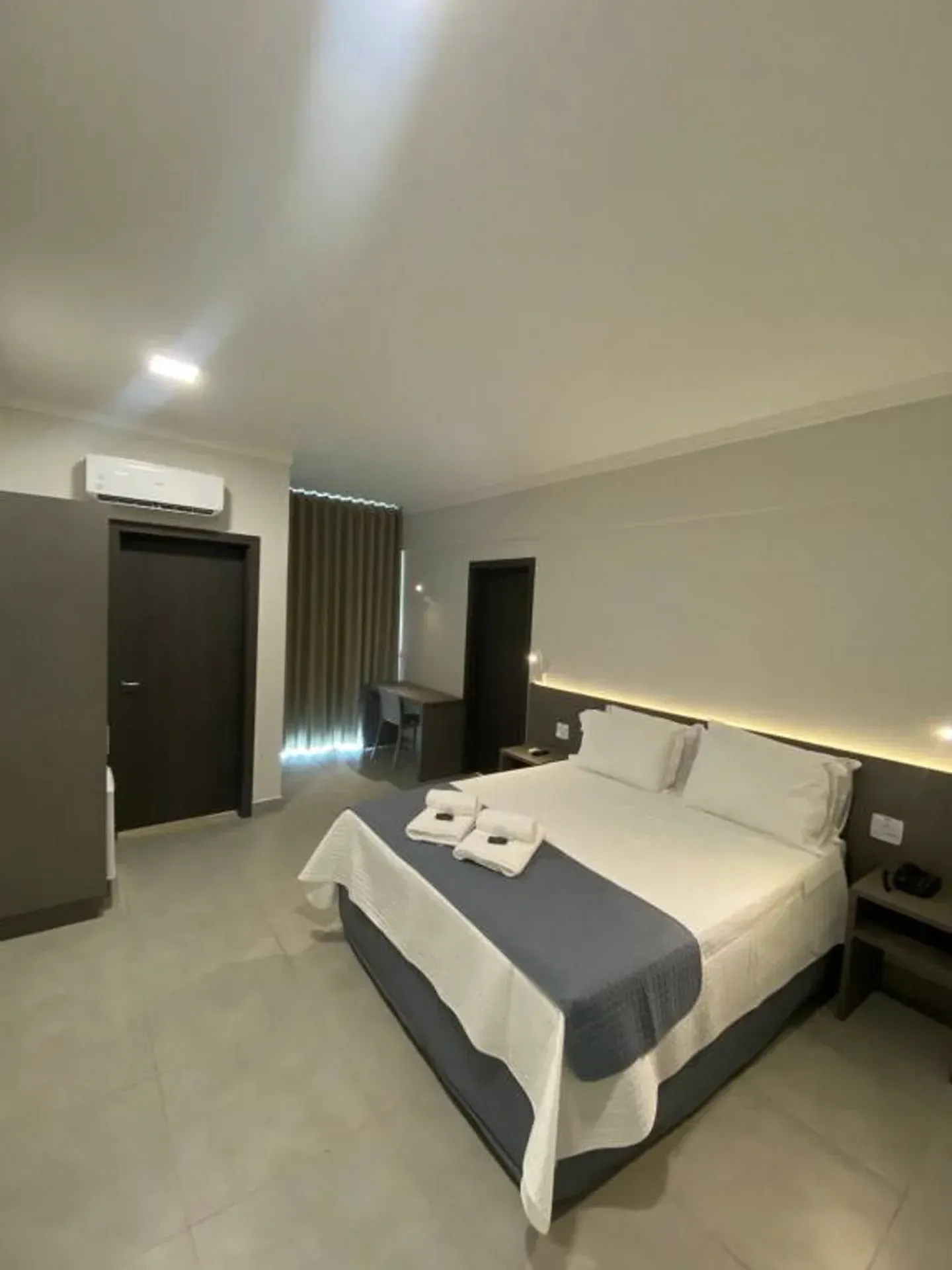 Quarto de hotel com cama, escrivaninha e detalhes em cinza.