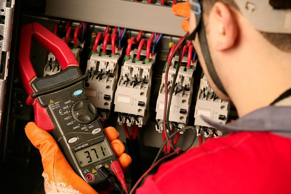An electrician is using a clamp meter to check a circuit board.