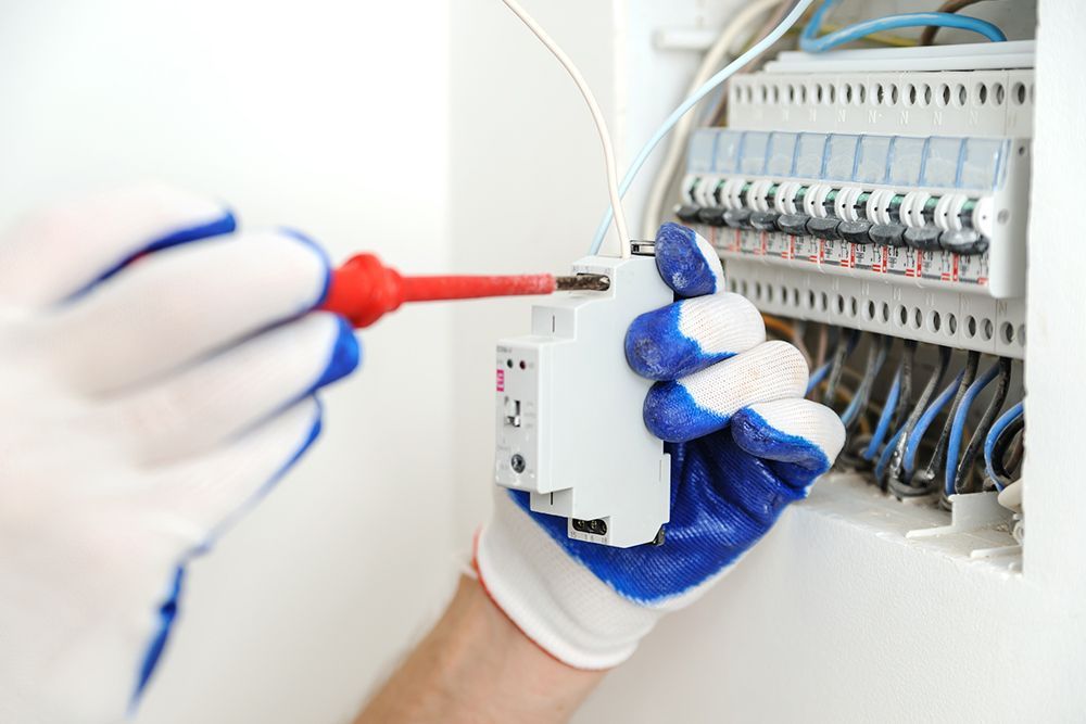 An electrician is working on an electrical box with a screwdriver.